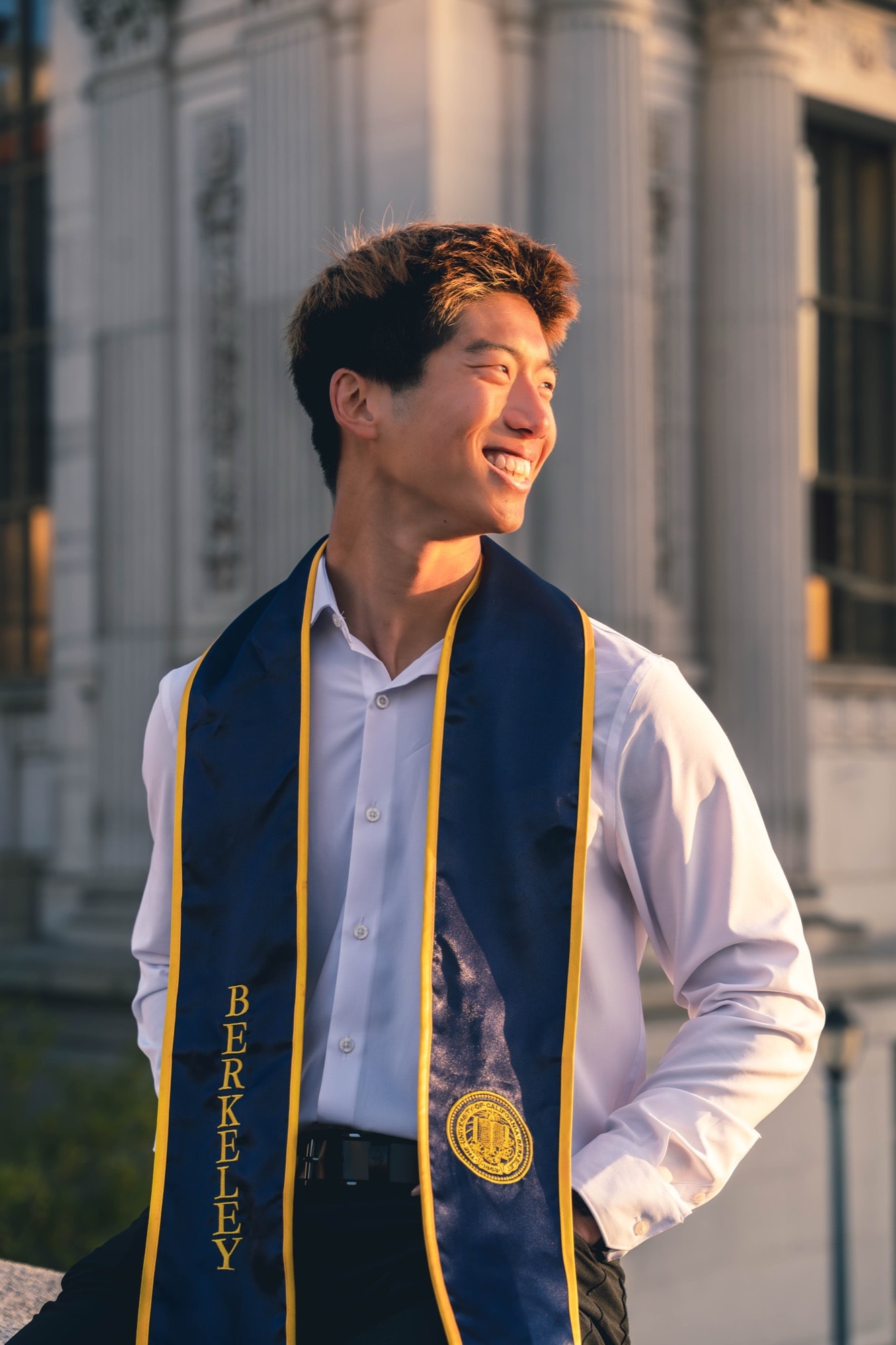 Graduate laughing in golden-hour light outside a campus hall