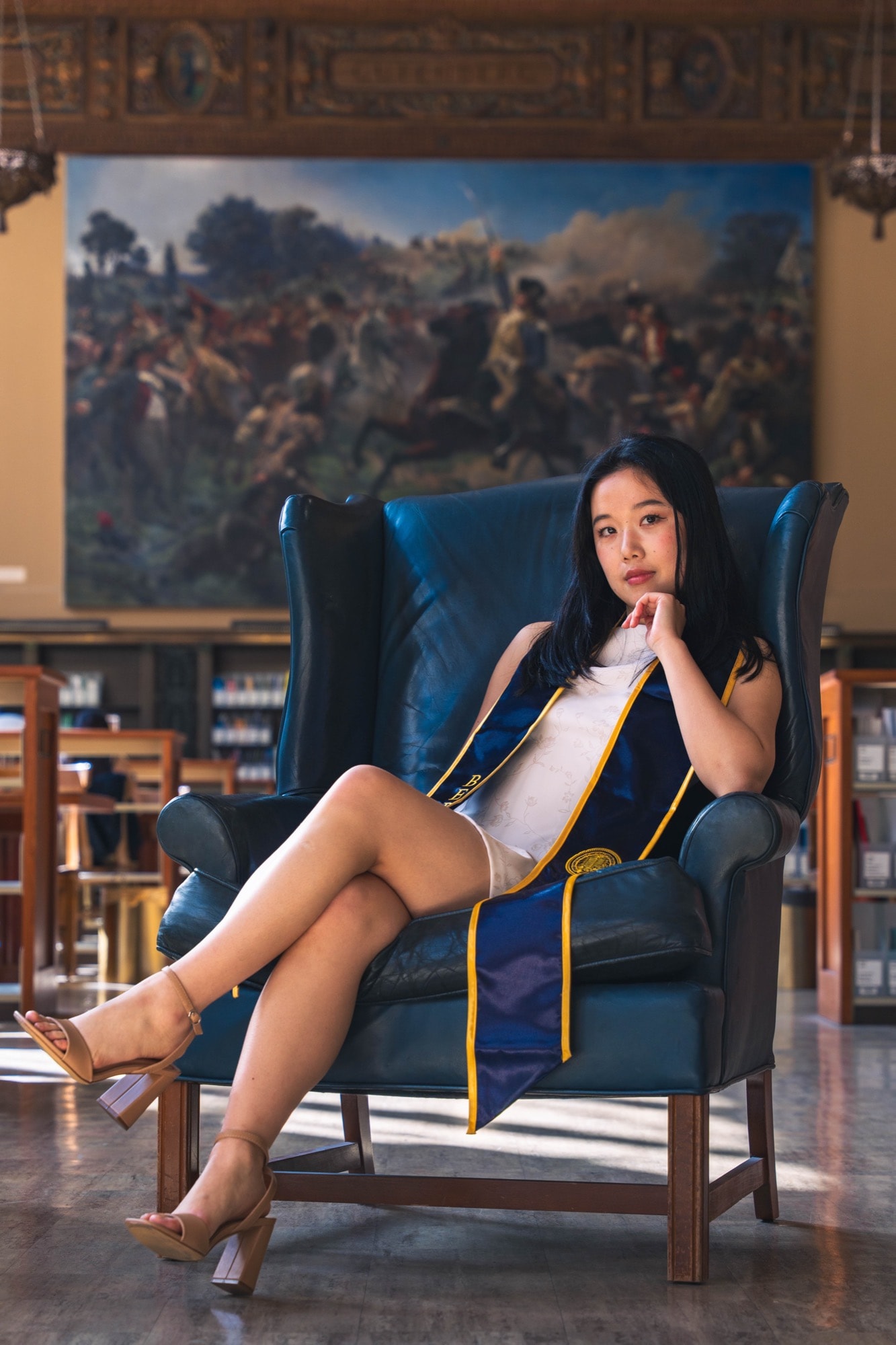 Graduate seated in a leather wingback chair in a grand library hall